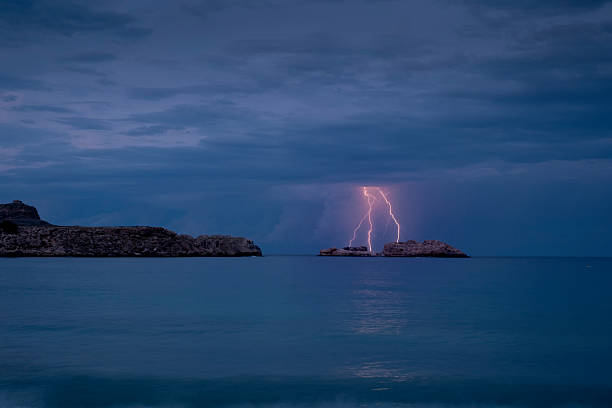 Lightning striking a small rocky island in the sea at night, illuminating a storm over rhodes