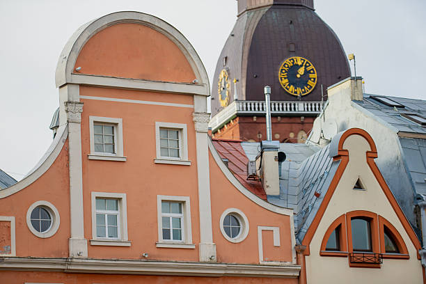 Foreground buildings with pastel facades and arched rooflines positioned below Riga Cathedral dome where clock face and structural elements are visible
