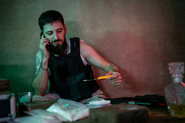istock Man In Tactical Vest On Phone While Handling Knife At Table With Paraphernalia 2248114393