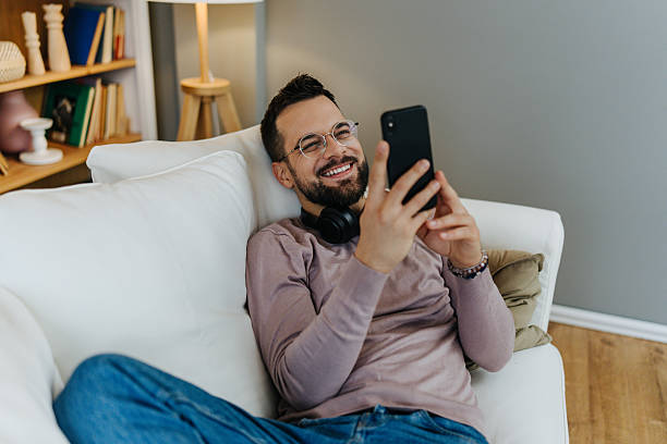 istock Smiling man relaxing on couch viewing phone 2248123631