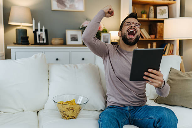 istock Excited man celebrating victory watching tablet at home 2248123676