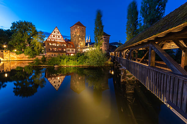 Illuminated Historic Old Town at Night. Weinstadel Building, Henkerbrucke Bridge and Henkerturm Tower. Pegnitz River. Reflection in Water. Nuremberg, Franconia, Germany. Wide Shot