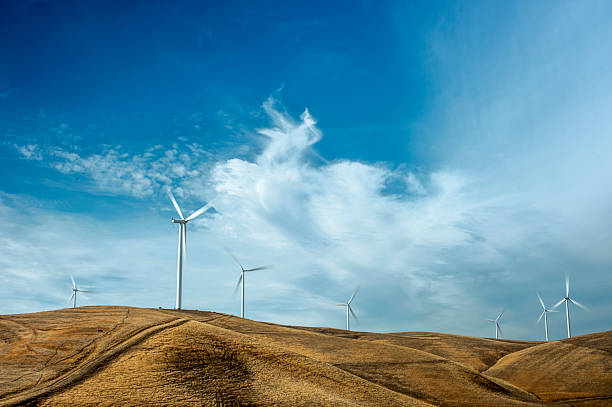Wind Turbines lined up along a coastal wind turbine farm, with clouds in background.