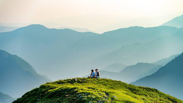 istock Two People Sitting on a Green Hill Overlooking a Misty Mountain Range 2248127762