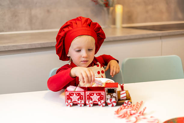 Child in red chef hat prepares colorful sweets on kitchen table during festive season