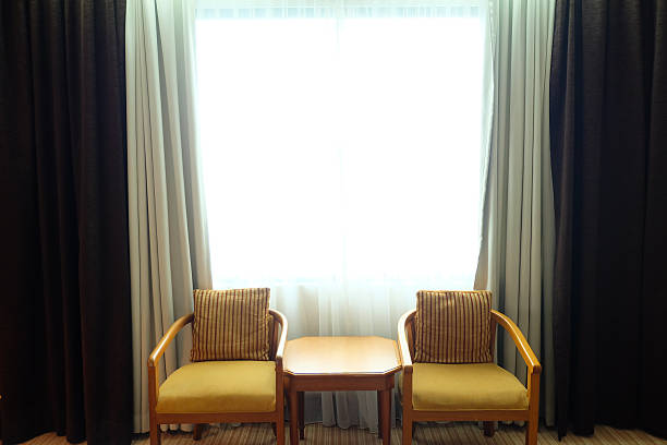 istock Two Comfortable Yellow Upholstered Chairs with a Small Wooden Table by a Bright Window Featuring Sheer and Dark Curtains in a Cozy Interior Room 2248139343