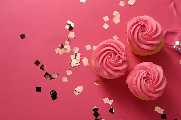 Delicious cupcakes with bright cream and confetti on pink background, flat lay. Space for text