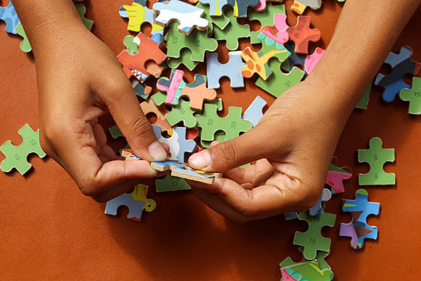istock Hands are assembling a jigsaw puzzle on a table. Colorful puzzle pieces are scattered, while fingers are focused on placing one piece in its proper position. 2248146950