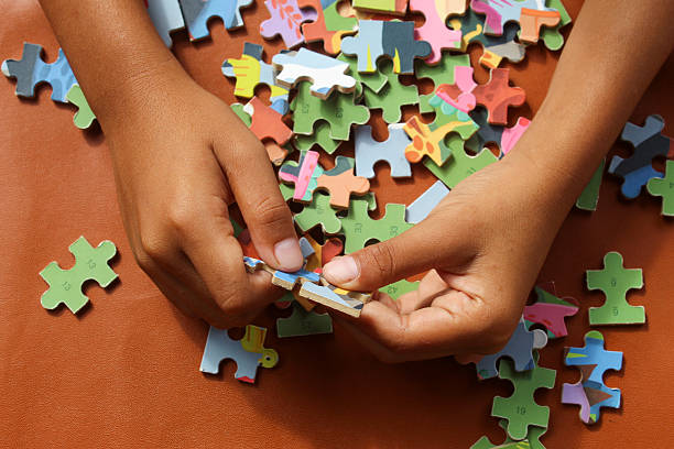 istock Hands are assembling a jigsaw puzzle on a table. Colorful puzzle pieces are scattered, while fingers are focused on placing one piece in its proper position. 2248146952
