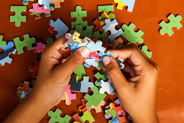 istock Hands are assembling a jigsaw puzzle on a table. Colorful puzzle pieces are scattered, while fingers are focused on placing one piece in its proper position. 2248146960
