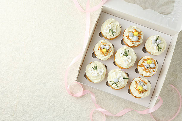 istock Tasty Easter cupcakes with vanilla cream in box and pink ribbon on beige table, flat lay. Space for text 2248152902