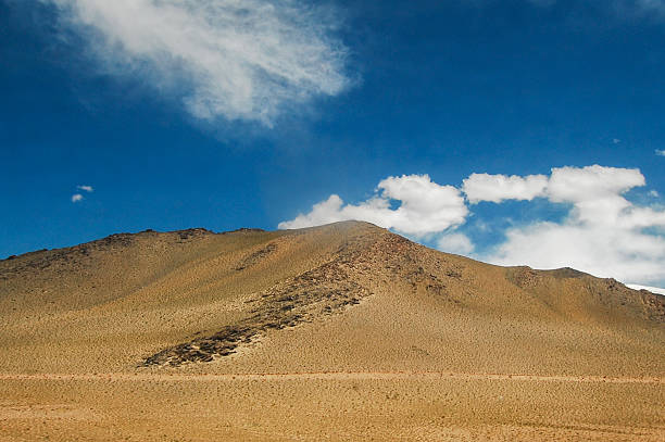 A vast arid mountain range under a clear blue sky with scattered clouds, showcasing a natural desert landscape.