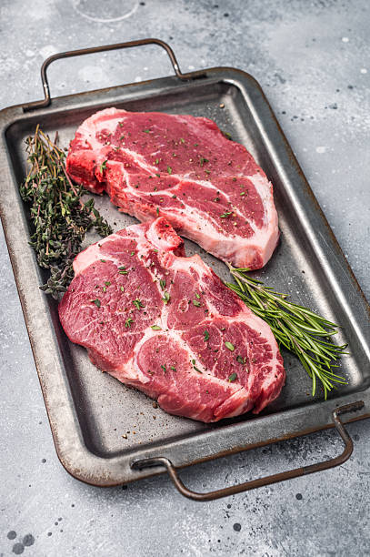 istock Raw pork neck meat steaks on steel tray. grey background. top view 2248157191