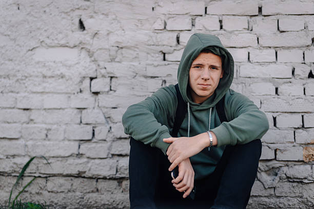 istock Young man in hoodie sitting by brick wall 2248157836