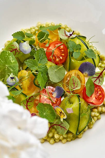 A beautiful gourmet couscous salad with burrata, vibrant cherry tomatoes, cucumber, and microgreens, served in a minimalist white bowl.