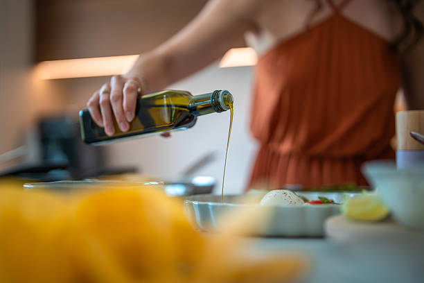 Woman In Rust-Colored Top Pouring Olive Oil While Preparing Dinner In Warmly Lit Kitchen