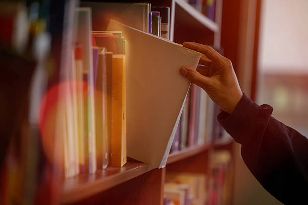 istock Hand picking book from library bookshelf for reading and education concept, symbolizing knowledge, education, learning, research, study, literature, academic resources in a quiet study environment 2248166603