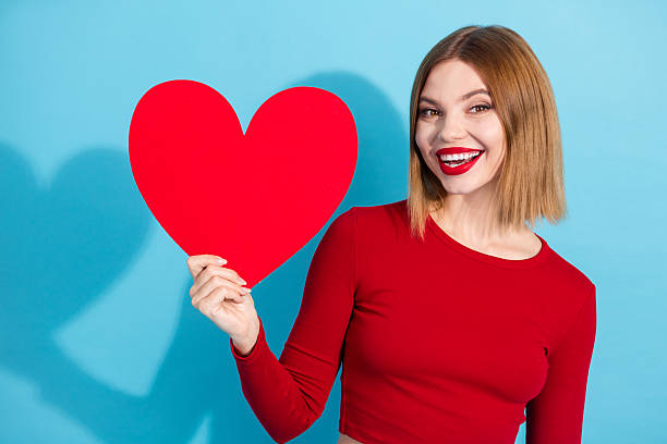 istock Cheerful young woman holding a bright red heart posing against a solid blue background in a stylish red top 2248171808