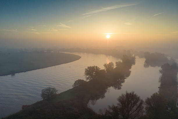 IJssel river meandering through the landscape during a foggy autumn morning near Zwolle and Hattem seen from above. A freight ship barge is sailing into the distance on the river IJssel in Overijssel, Netherlands during an autumn sunrise.