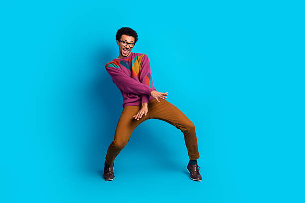 A lively and expressive young man dressed in fashionable casual clothing poses dynamically against a bold blue backdrop, exuding energy and charm