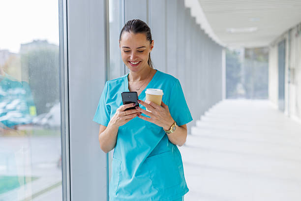 istock Female healthcare worker smiling while using smartphone drinking coffee 2248177402