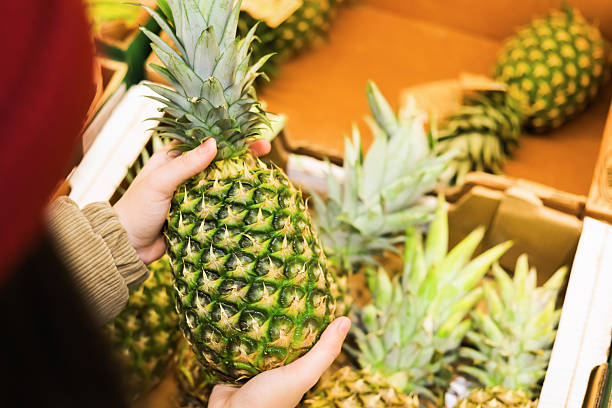 istock A hand selects a fresh, spiky pineapple from a wooden crate display in the produce section of a grocery store. 2248178302