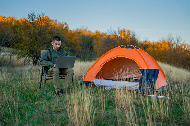 istock Young man on a mountain surrounded by camping gear and a tent, sitting outdoors and browsing the internet on a laptop. Concept of remote work, connection to nature, online productivity, and modern outdoor lifestyle. 2248178438