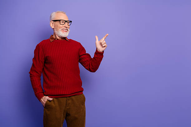 istock Mature man in red sweater points with smile against violet background for lifestyle advertising and fashion 2248179122