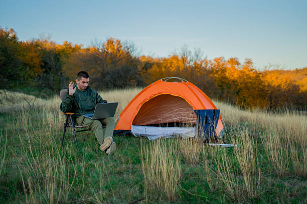 istock Young man on a mountain surrounded by camping gear and a tent, sitting outdoors and browsing the internet on a laptop. Concept of remote work, connection to nature, online productivity, and modern outdoor lifestyle. 2248179177