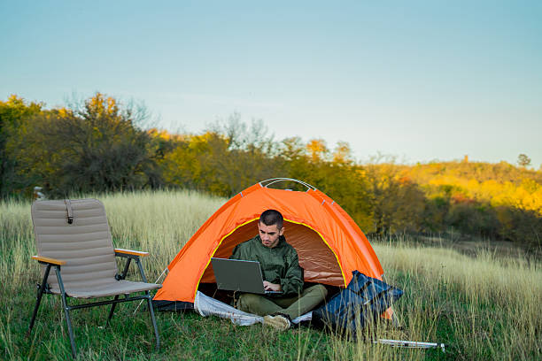 istock Young man on a mountain surrounded by camping gear and a tent, sitting outdoors and browsing the internet on a laptop. Concept of remote work, connection to nature, online productivity, and modern outdoor lifestyle. 2248180280