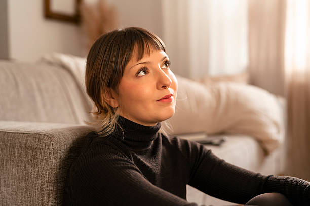 istock Contemplative woman seated by a sofa in a cozy home setting, lost in thought and reflection 2248180606