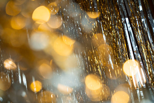 Holographic festive background with shiny tinsel and glitter. Gold and silver bokeh create a New Year and Christmas celebration mood. Perfect metallic, colorful holiday texture.