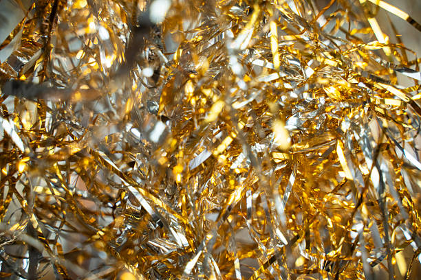 Macro view of shimmering gold and olive tinsel, capturing the fine metallic strips reflecting light. The sharp detail contrasts beautifully with the soft, glowing bokeh background, making it ideal for celebratory, Christmas, or New Year's Eve promotional materials.