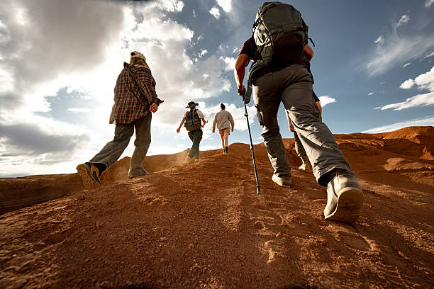 Group of young hikers walks uphill at sunset desert. Close up photo of tourist legs against sunset sky