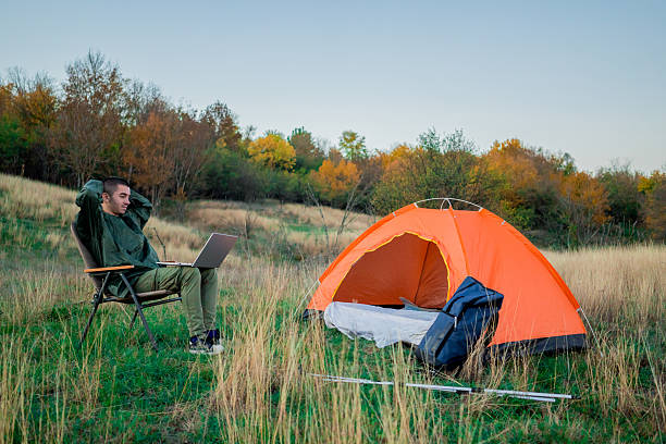 istock Young man on a mountain surrounded by camping gear and a tent, sitting outdoors and browsing the internet on a laptop. Concept of remote work, connection to nature, online productivity, and modern outdoor lifestyle. 2248182149