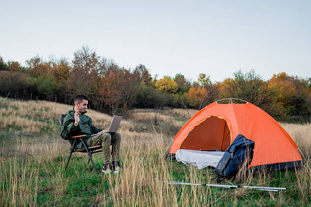 istock Young man on a mountain surrounded by camping gear and a tent, sitting outdoors and browsing the internet on a laptop. Concept of remote work, connection to nature, online productivity, and modern outdoor lifestyle. 2248182742