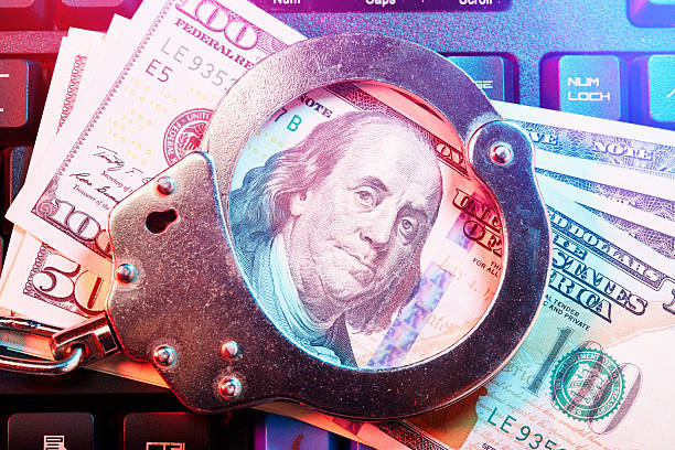 istock Metal handcuffs and some American One hundred dollar banknotes on computer keyboard, internet cyber crime concept 2248183283