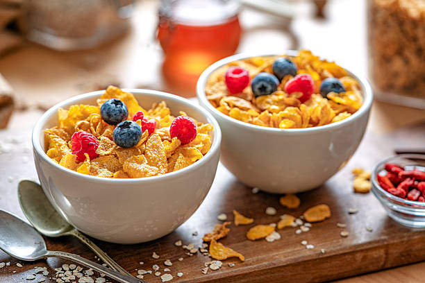Two bowls filled with corn flakes and berry fruits on dining table. Breakfast cereal or healthy eating or dieting. Food high in dietary fiber for healthy bowel or digestive system