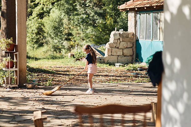 Child sweeping scattered leaves on a sunny day in a rustic yard