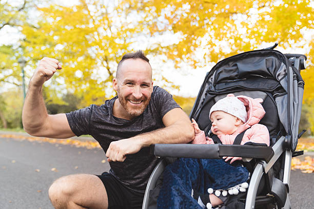 A man with her daughter standing in jogging stroller outside in autumn nature