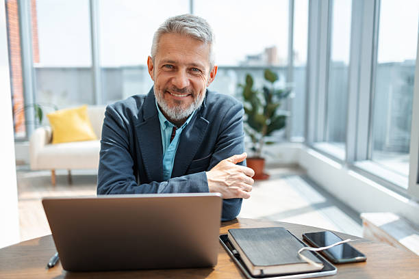 istock Confident senior businessman smiling while working on laptop in modern office 2248190391