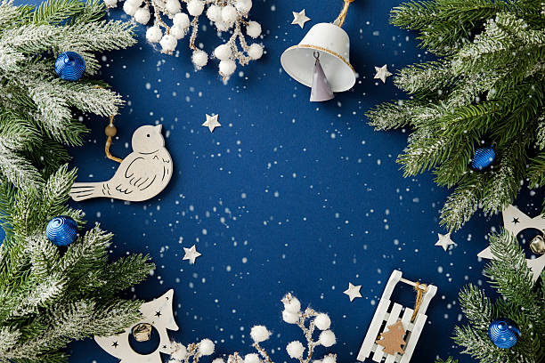 Rustic wooden Christmas bird, sled, and bell ornaments frame a deep blue background with falling snow