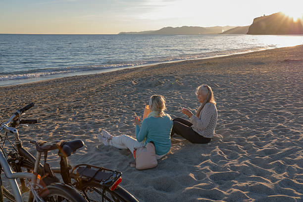 istock Senior women eat oranges on beach at sunset 2248192891