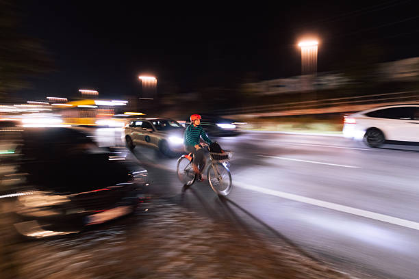 Berlin, Germany – September 27, 2025: A cyclist rides along a busy multi-lane road at night. Cars and street lighting create strong motion blur, illustrating urban nighttime movement.