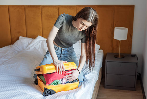 istock Young woman struggling with overstuffed suitcase on bed 2248201883