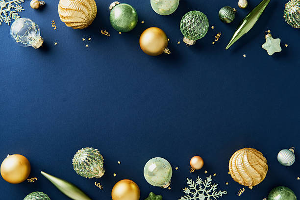 Gold and green Christmas baubles frame on navy background with copy space.
