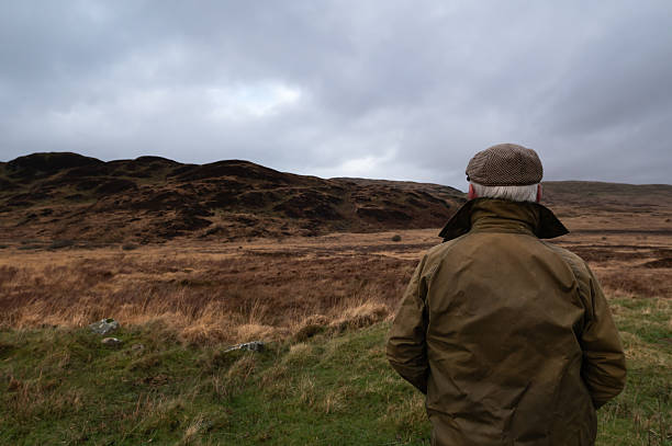 Senior farmer looking at livestock grazing on a distant hill in a remote rural location in Scotland