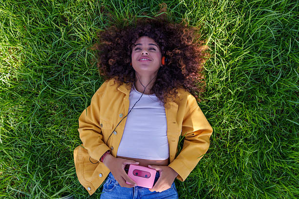 Woman lying on green grass enjoying music with headphones and a vintage cassette player. Feeling relaxed in a park setting