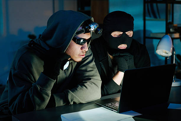 istock Two Young Adult Men Wearing Masks Hacking Computer in Office at Night 2248211571