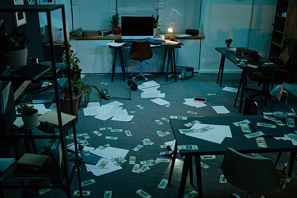 Office scene showing scattered documents and money on floor with overturned chair and disarrayed furniture indicating recent theft or burglary in modern workspace